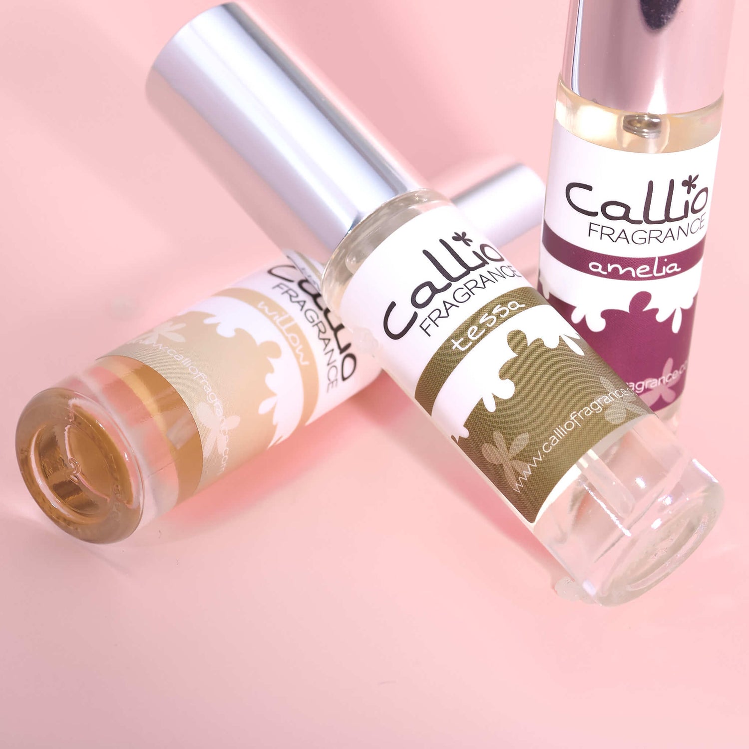 Bottles of Willow, Tessa, and Amelia Travel-size perfume on a light pink background.