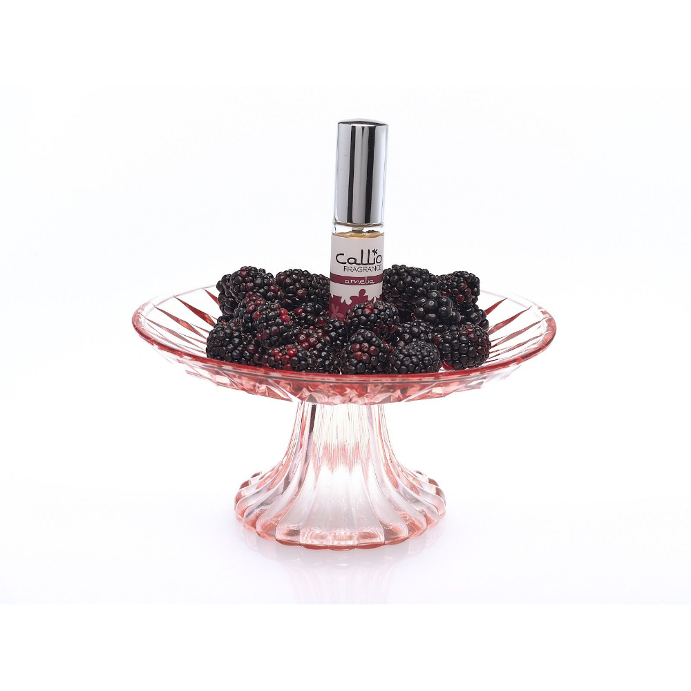 Image of a bottle of Amelia Travel-Size Perfume Spray by Callio Fragrance on a pink pedestal, surrounded by blackberries on a white background.