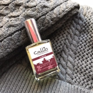 Bottle of Amelia one-ounce perfume lying on a gray scraf and hat.