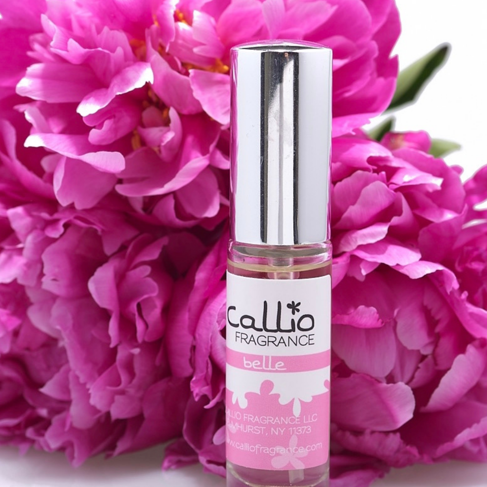 Travel size Belle perfume spray on a white background with three bright pink peonies.