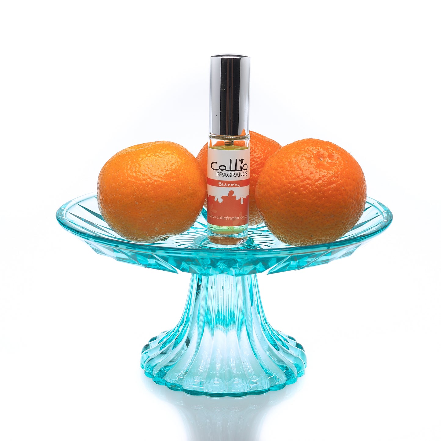 Sunny Travel Perfume Spray on a teal cakestand with 3 mandarin oranges on a white background.