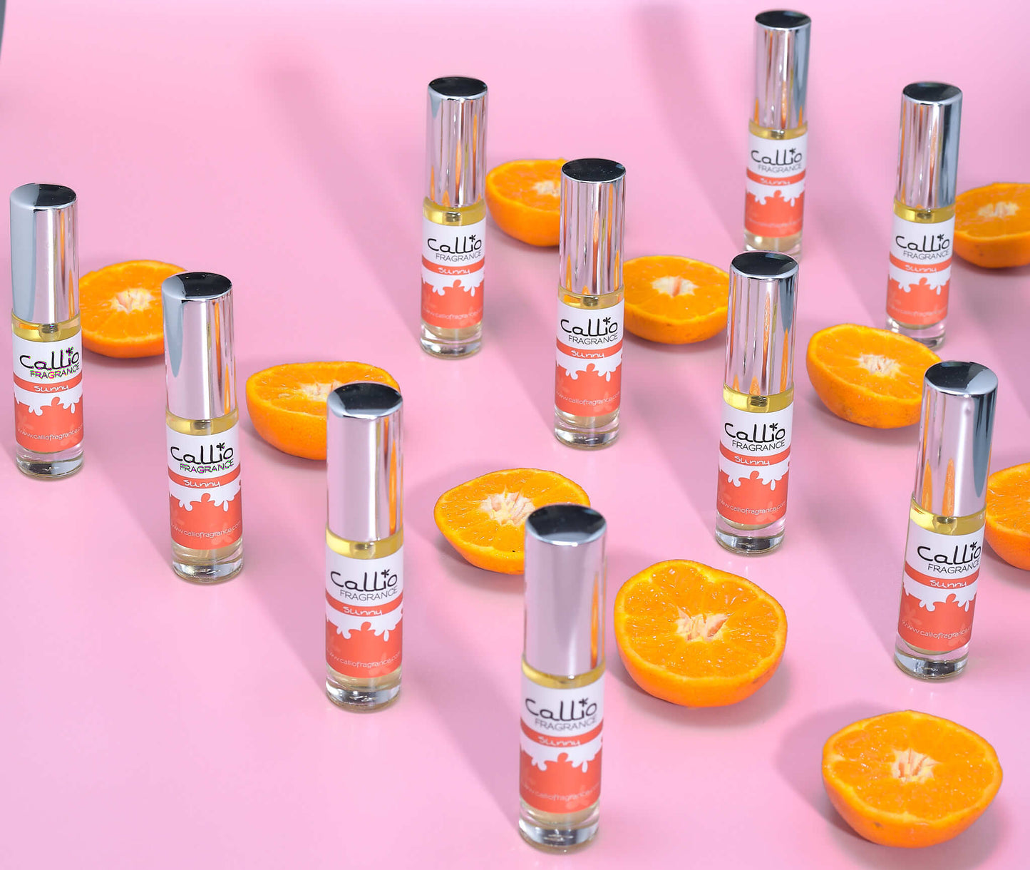 10 bottles of Sunny Travel Perfume Spray on a pink background with halves of mandarin oranges.